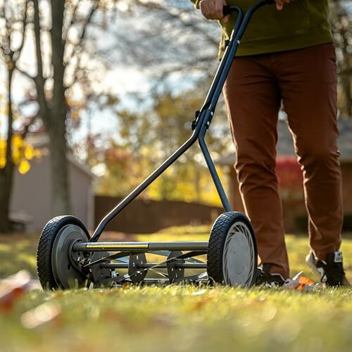 Person pushing a manual lawn mower on grass